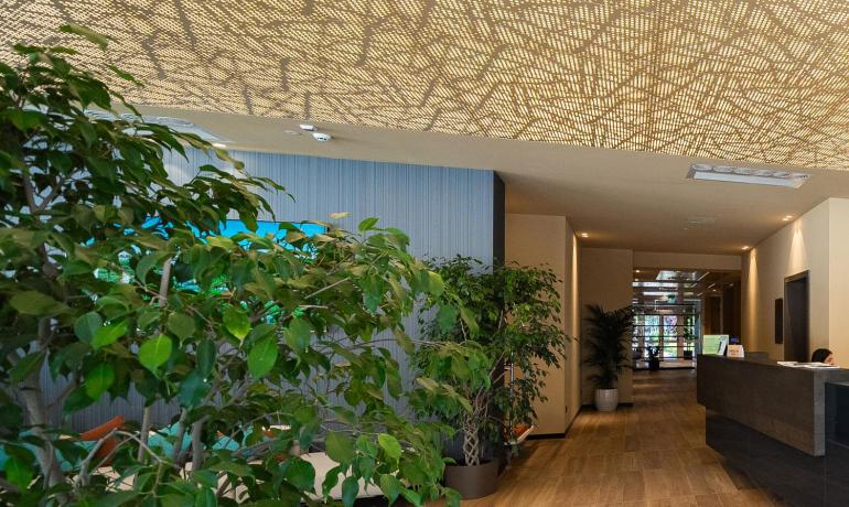 Elegante Lobby mit perforierter Decke, sanfter Beleuchtung und üppigen grünen Pflanzen.