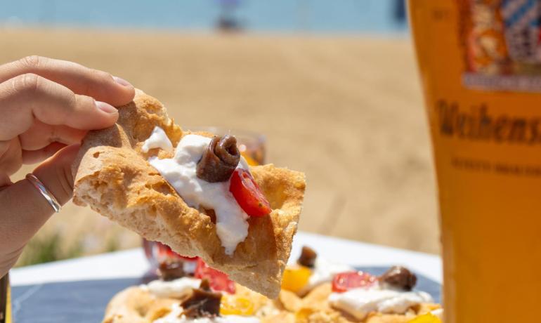 Gourmet pizza on the beach with refreshing beer, sun, and sea.