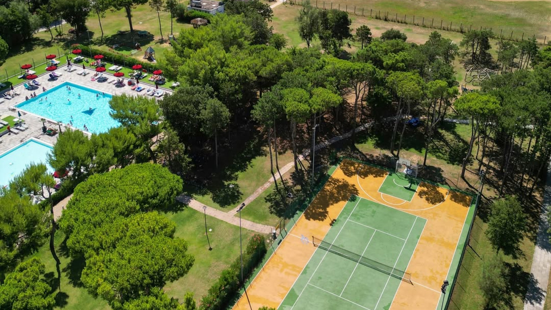 Pool and sports court surrounded by greenery.