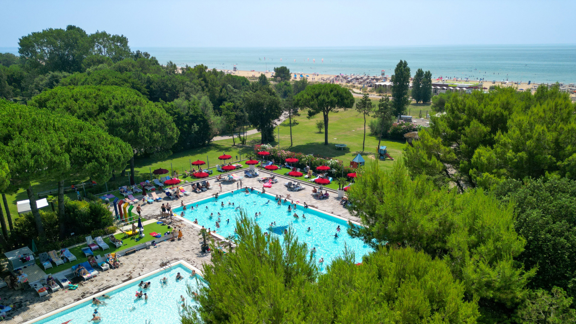 Piscina e spiaggia circondate da alberi, vista mare.