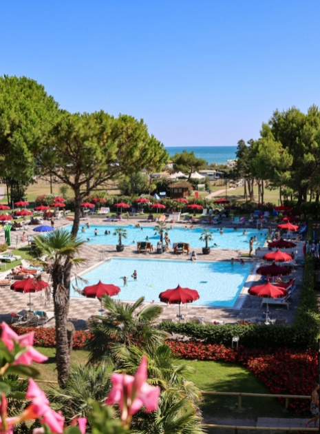 Freibad mit roten Sonnenschirmen, umgeben von Bäumen und Meerblick.