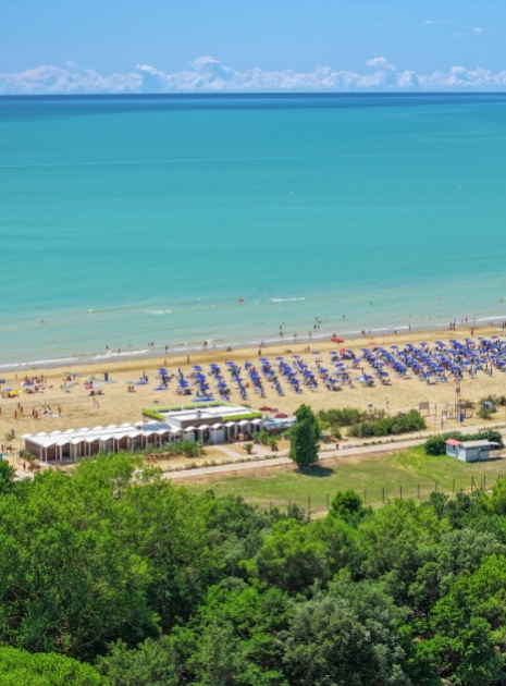 Sandstrand mit blauen Sonnenschirmen und türkisfarbenem Meer, von oben gesehen.