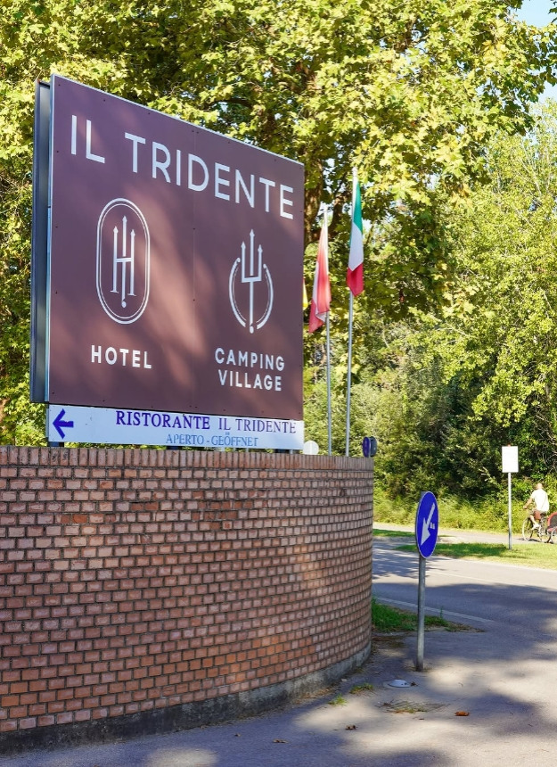 Entrance of Camping Village Il Tridente with flags and signage.