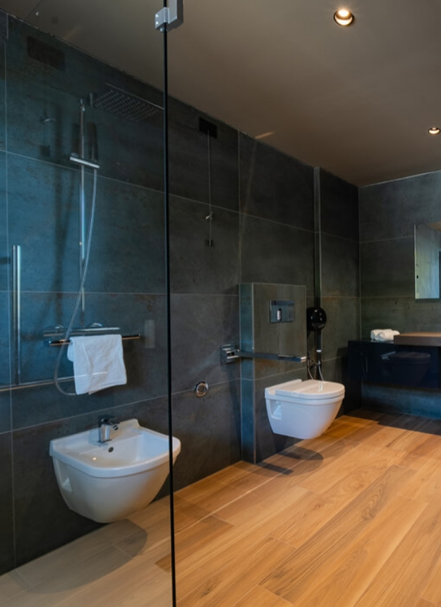 Modern bathroom with shower, bidet, and sink on wooden floor.