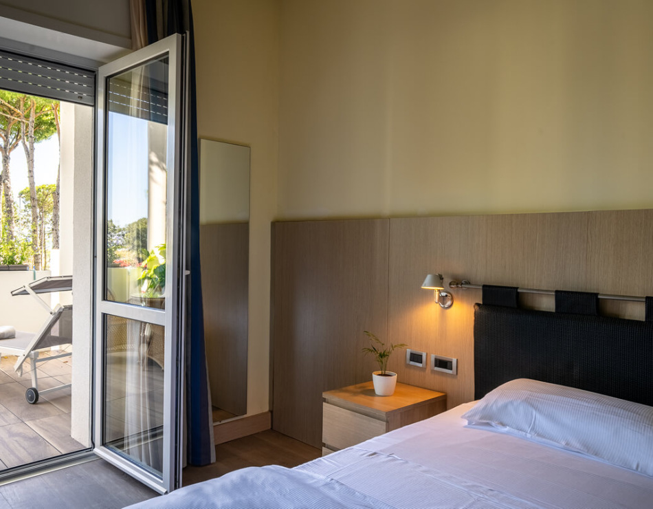 Helles Zimmer mit Terrasse, Liegestuhl und Blick auf Bäume.